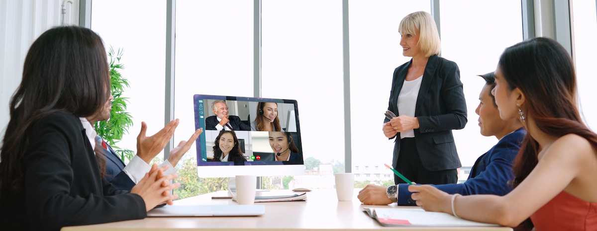 Five team members seated at a table in discussion with four team members pictured on a computer monitor